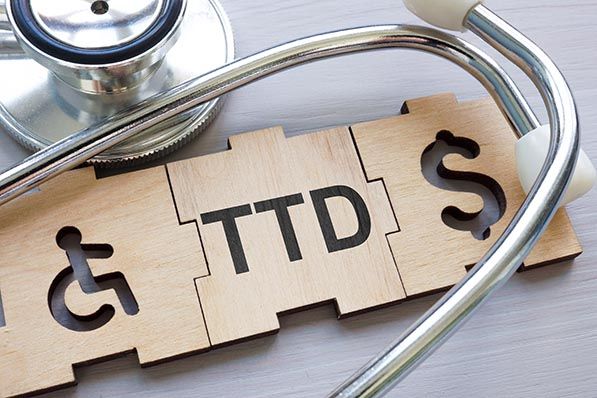 A stethoscope surrounds wooden puzzle pieces marked with a wheelchair symbol, TTD and a dollar sign.