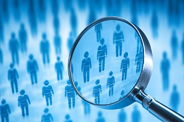 A magnifying glass enlarges several blue human figures in a grid of people icons.