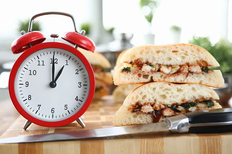 A red alarm clock stands beside stacked toasted sandwiches on a kitchen counter.
