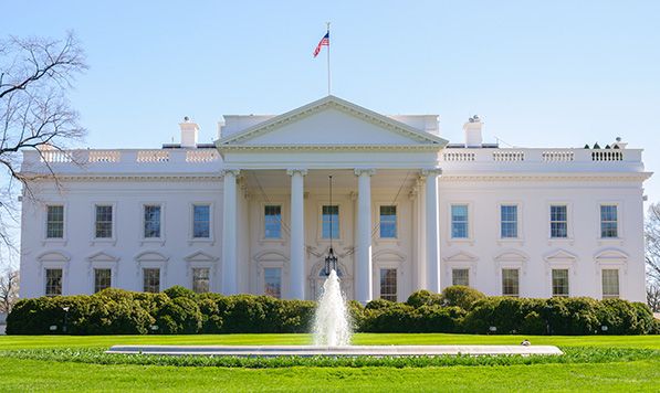 The White House behind a fountain, trimmed hedges and a green lawn.