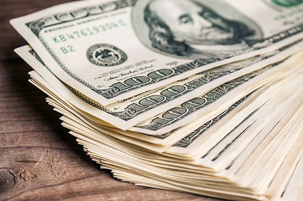 A thick stack of U.S. hundred-dollar bills rests on a wooden surface.