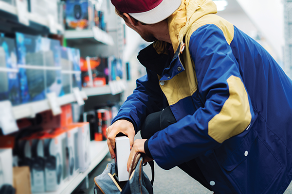 A person in a blue-and-yellow jacket places a boxed item into a bag in a store aisle.