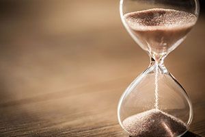 Sand runs through a glass hourglass on a wooden surface.