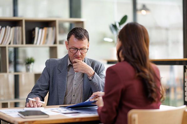 Two colleagues review documents across an office desk.