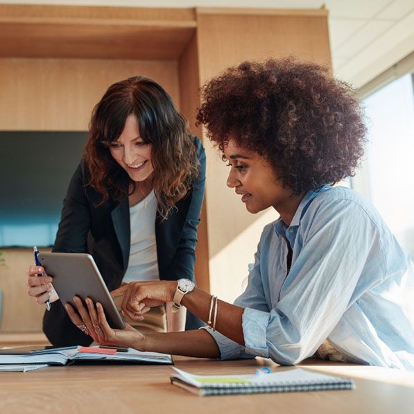 Two women review a tablet together at an office table.