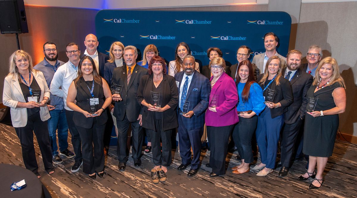 A large group poses before a CalChamber backdrop, several holding glass awards.