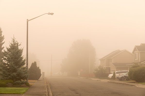 A residential street and houses are obscured by dense orange-gray smoke.