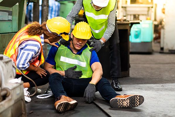 Workers wearing safety vests and hard hats assist a coworker seated on the floor.
