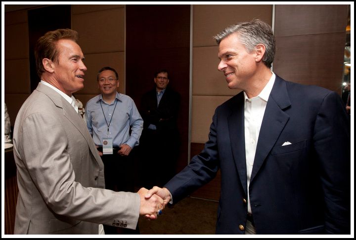 Two men shake hands indoors as two other men watch in the background.