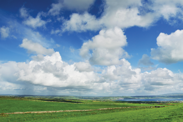 Green fields stretch toward distant hills under a blue sky filled with white clouds.