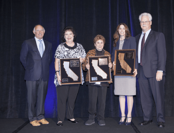 Five people pose onstage, with three holding framed California awards.