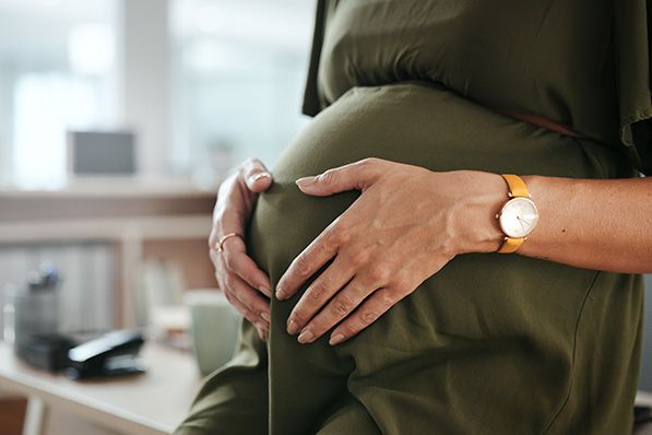Close-up of a pregnant person's hands resting on their belly over a green dress.