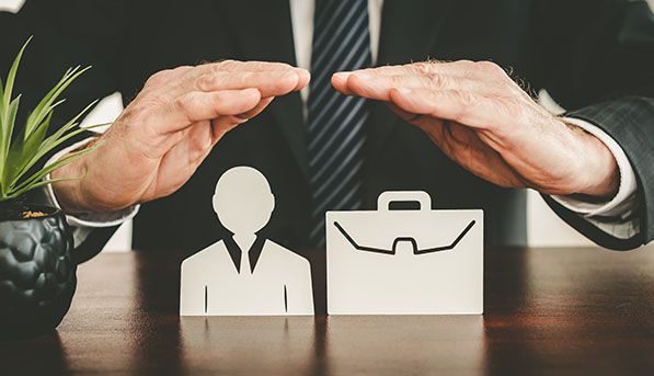 Hands form a protective arch over paper cutouts of a person and briefcase.