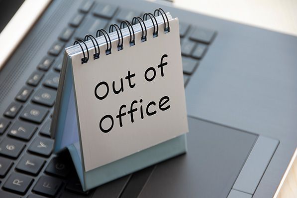 A spiral desk sign reading Out of Office sits on a laptop keyboard.