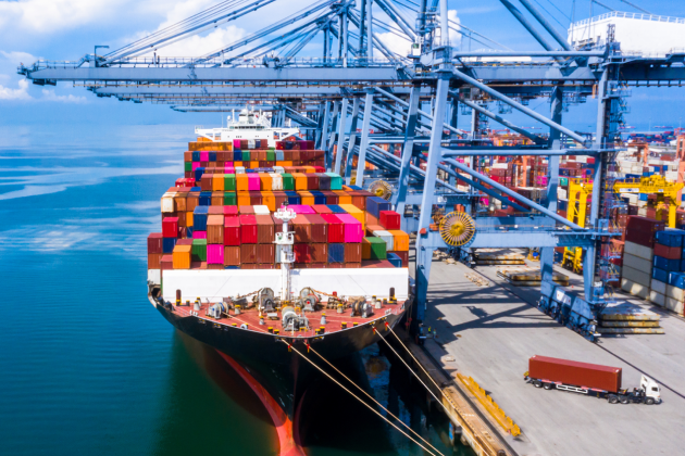 Container ship loaded with colorful cargo beside cranes at a port.