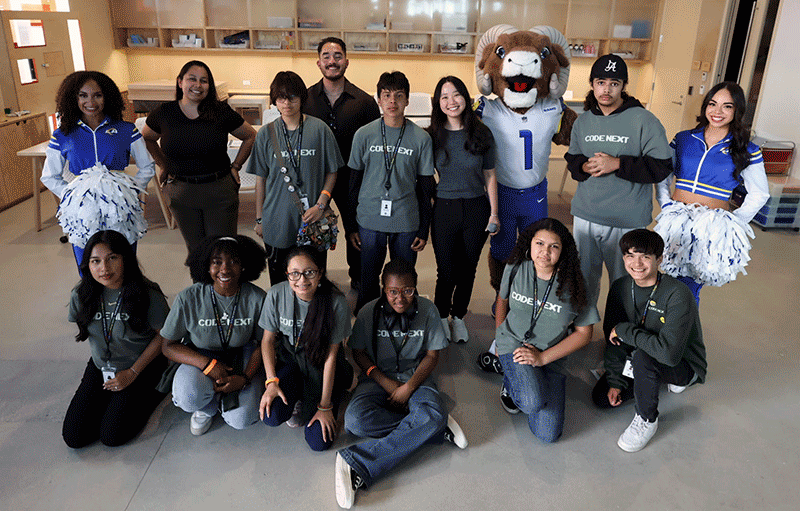 A group poses with cheerleaders and a costumed mascot at an indoor gathering.