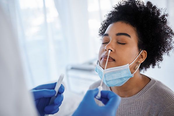 A healthcare worker takes a nasal swab from a woman with her mask lowered.