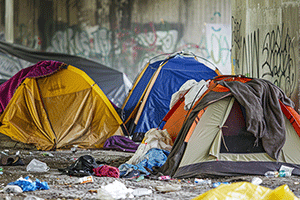 Colorful tents and scattered belongings line a graffiti-covered wall.