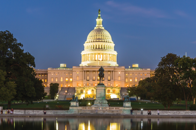 The illuminated United States Capitol at dusk, reflected in a pool.