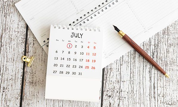 A July desk calendar with the first circled lies beside notebooks and a pencil.