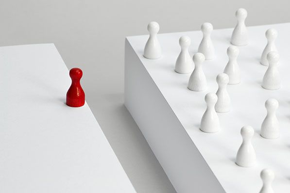 A single red game piece stands apart from a group of white pieces on a raised platform.