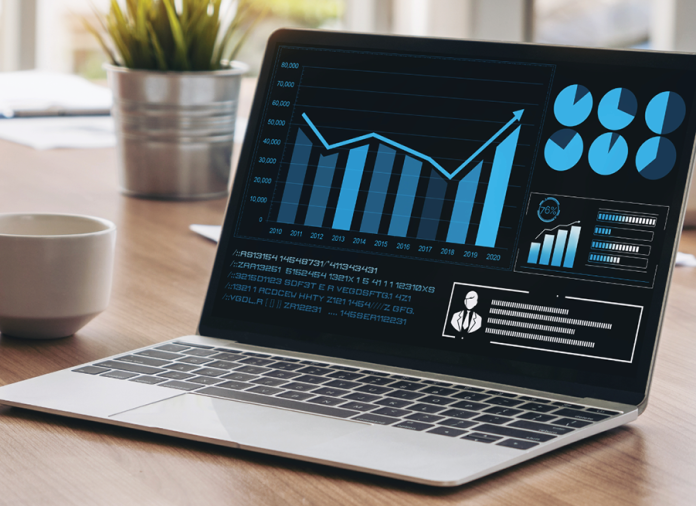 A laptop displays blue financial charts and graphs on a wooden desk.