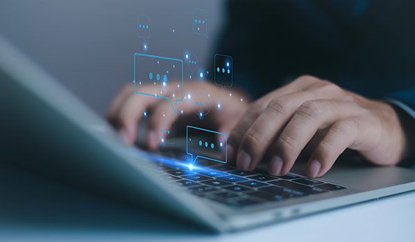 Hands typing on a laptop with illustrated chat bubbles floating above the keyboard.
