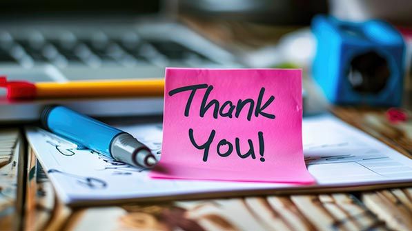 A pink sticky note reading Thank You! rests among office supplies on a desk.