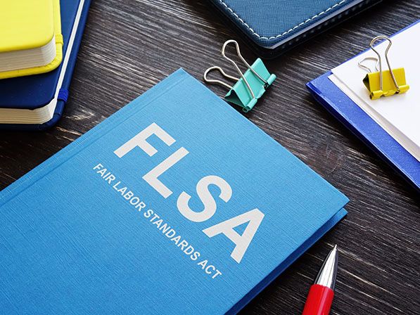 Blue booklet labeled FLSA Fair Labor Standards Act on a desk with stationery.