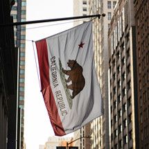 A California Republic flag hangs from a building along a city street.