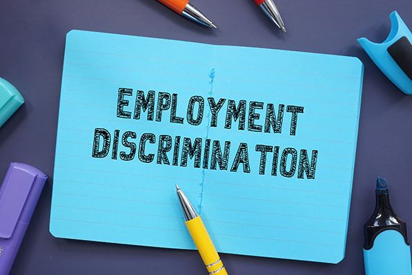 Blue notebook labeled EMPLOYMENT DISCRIMINATION surrounded by pens and highlighters.