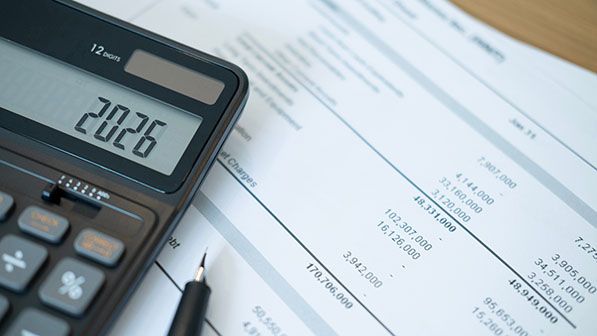 A calculator displaying 2026 rests on financial documents beside a pen.