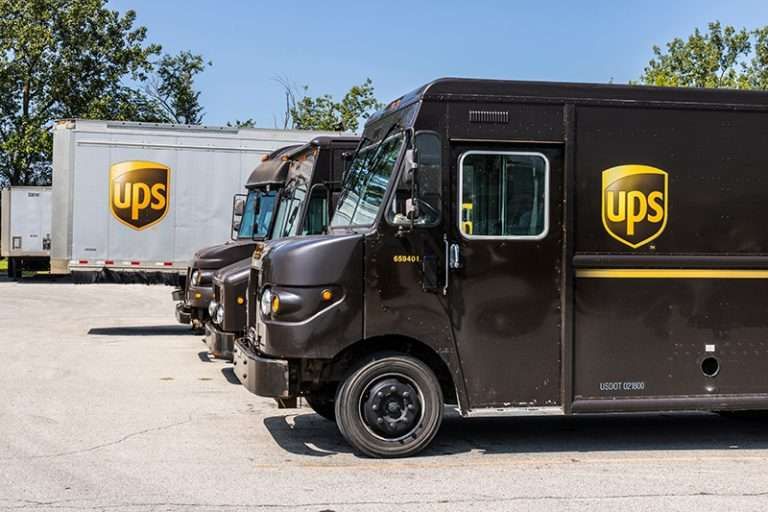 A row of brown UPS delivery trucks and a white UPS trailer parked.