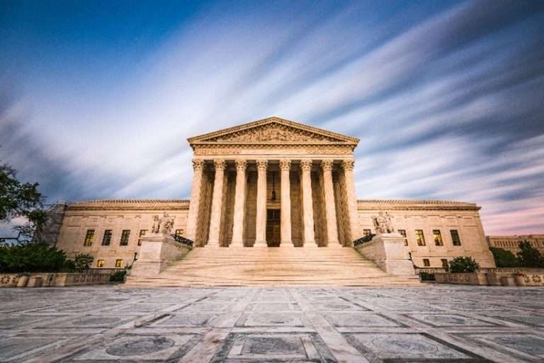 The US Supreme Court building with its neoclassical facade, columns, and steps under a streaky sky.