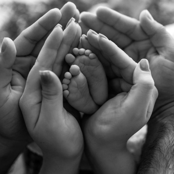 Black-and-white close-up of adult hands cupping a baby’s feet.