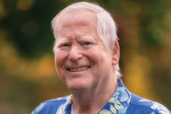 Portrait of a smiling white-haired man in a blue patterned shirt outdoors.