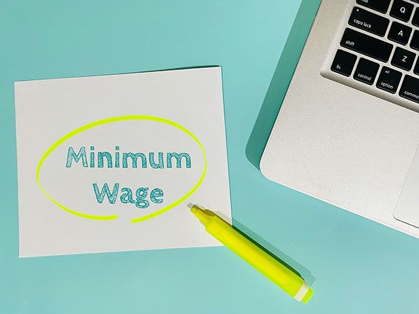 Minimum Wage written on a note and circled in yellow beside a laptop and highlighter.