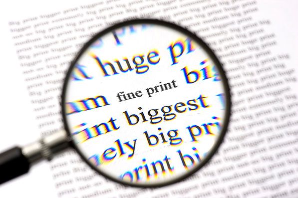 A magnifying glass enlarges the words fine print on a printed page.