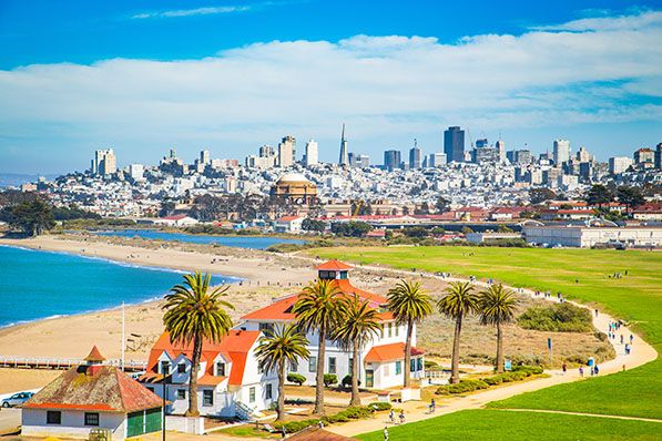 San Francisco waterfront park, palm trees and red-roofed buildings with the city skyline beyond.