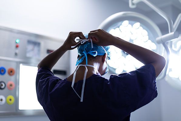 A healthcare worker ties a surgical cap beneath bright operating-room lights.