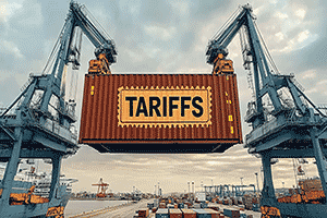 Port cranes lift a shipping container labeled TARIFFS.