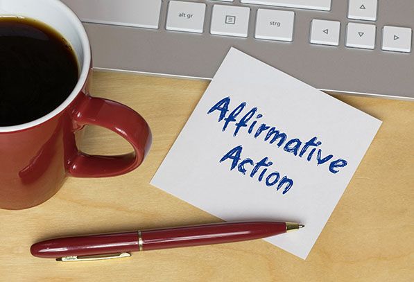 A note reading Affirmative Action lies beside a coffee cup, keyboard and pen.