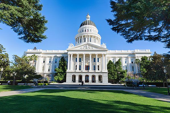 The California State Capitol framed by trees above a green lawn.
