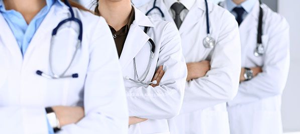 A group of healthcare workers in white coats with stethoscopes stand with folded arms.