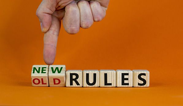 A finger turns a wooden block from OLD to NEW beside blocks spelling RULES.