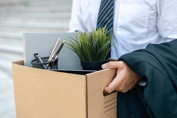 A person carries a cardboard box filled with office supplies, a laptop and a plant.