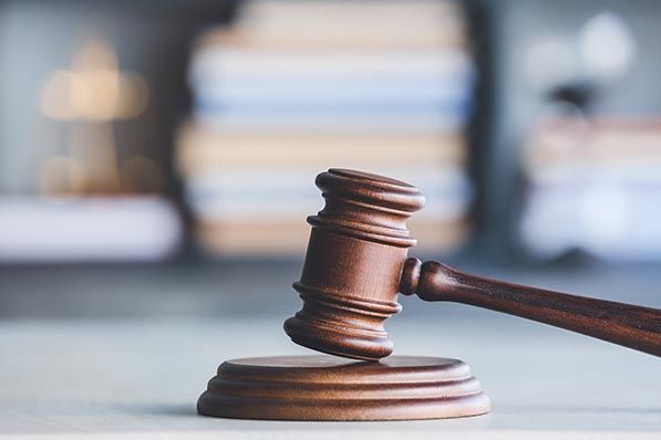 A wooden judge’s gavel rests against its sound block on a desk.