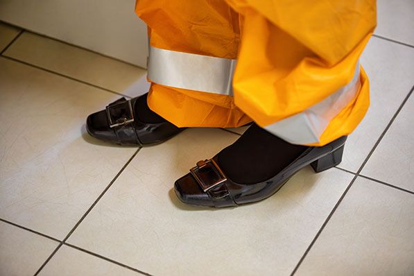 Close-up of black shoes below bright orange work trousers with reflective bands.