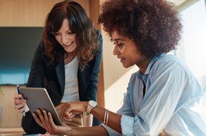 Two women smile while reviewing a tablet together.