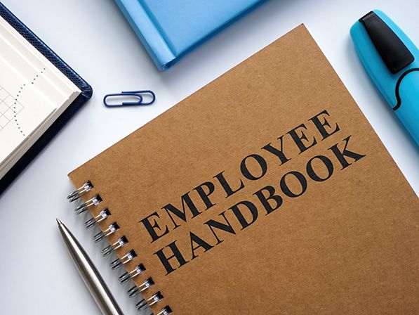 Brown spiral-bound Employee Handbook on a desk with stationery.